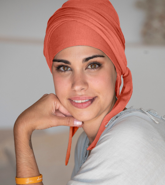 mujer joven sonriendo con un pañuelo oncológico coral