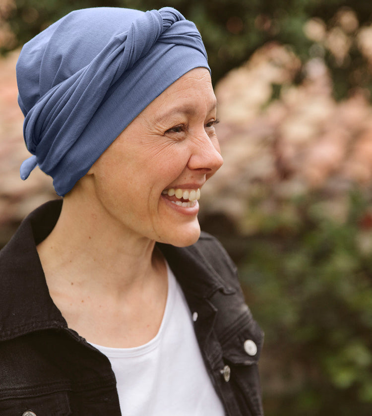 Mujer sonriente con pañuelo oncológico azul de iBBIBBI, confeccionado en tejido suave y transpirable. Diseño cómodo y estiloso para el día a día.